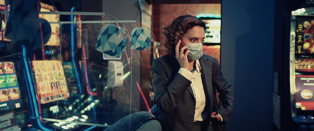 A woman in a face mask talks on a cellphone, surrounded by digital screens