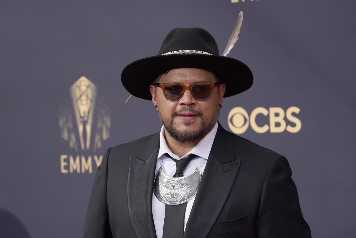 Sterlin Harjo in a black brimmed hat and black suit and tie.