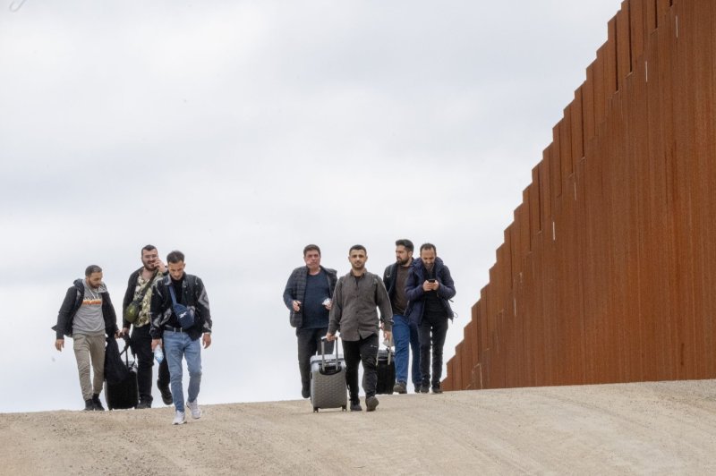 Migrants walk along the United States side of the border wall with Mexico to surrender to the U.S. Border Patrol near Campo, Calif., on March 13. The State Department on Tuesday expanded a visa-restriction policy to target travel agencies and tour operators that facilitate irregular migration. Photo by Pat Benic/UPI