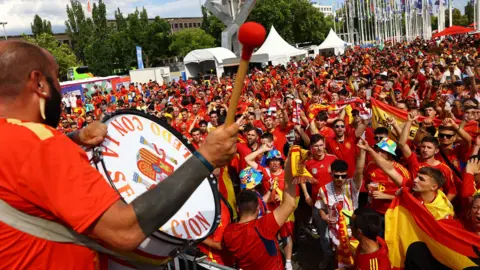 Reuters Spain fan plays a drum in front of a crowd of Spanish fans wearing red and yellow