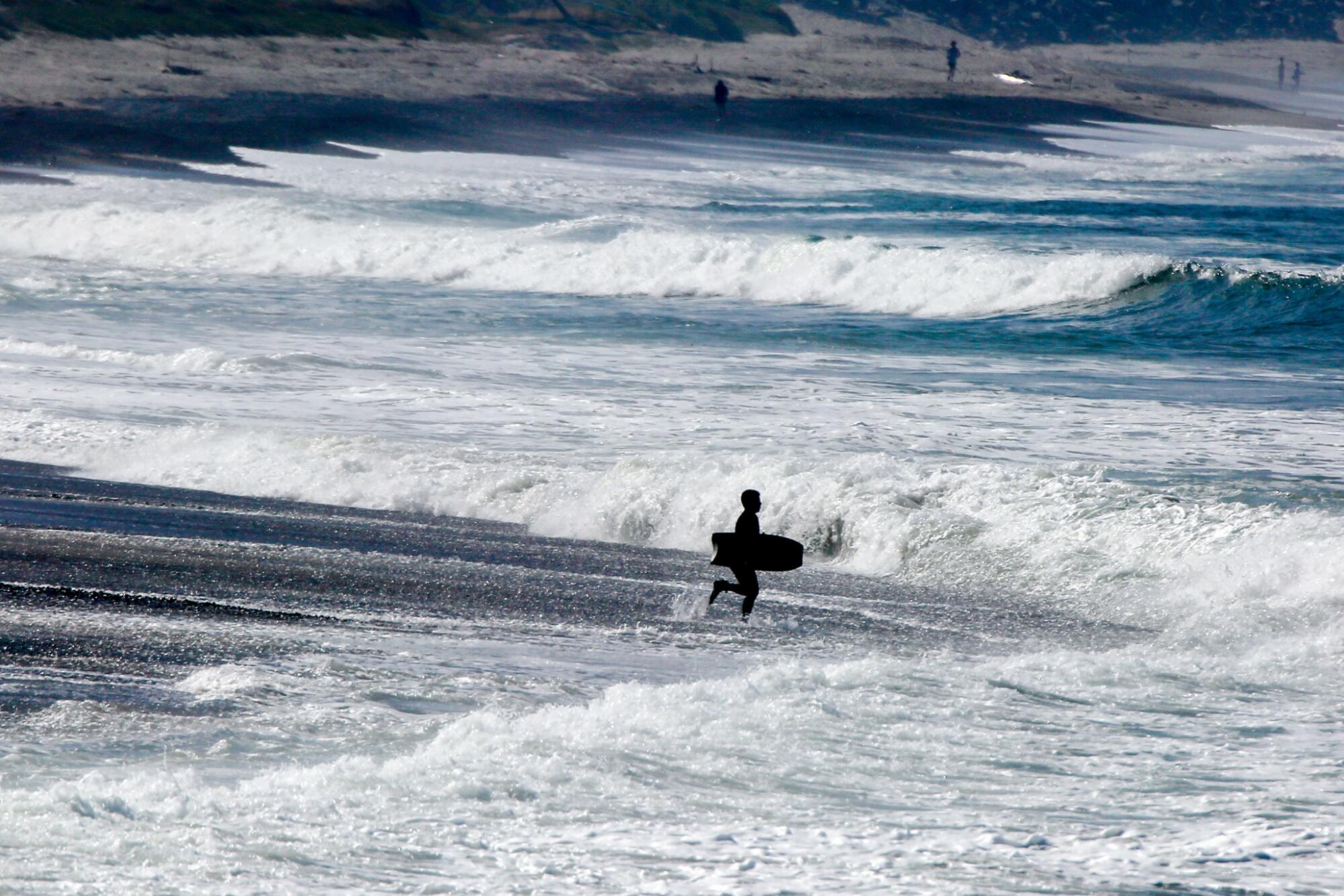 A Boogie boarder enters blue water with white waves.