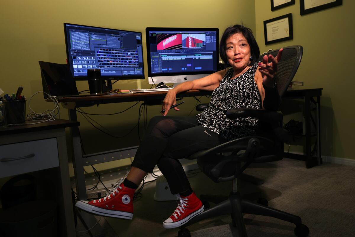 A woman sitting in a swivel chair at a desk with two monitors and an editing software on the screen.