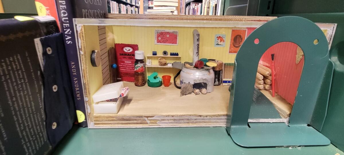 A mini kitchen diorama fashioned out of found objects, doll-like toys and bookends.