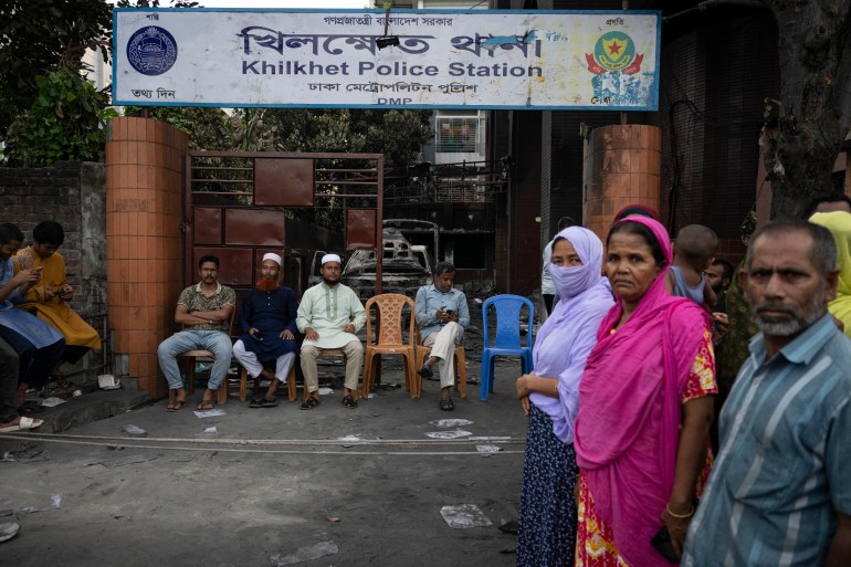 People keep guard in front of a police station which was vandalised on Monday, in Dhaka