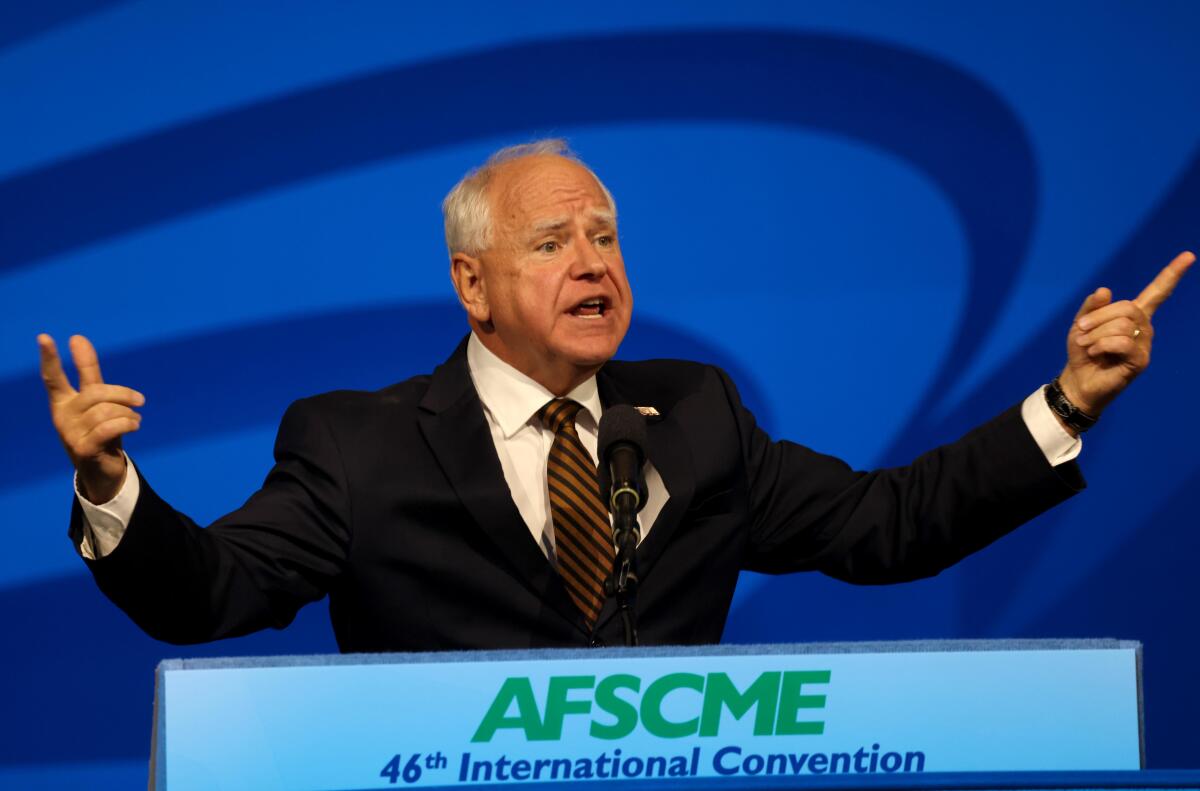 Tim Walz gestures as he speaks against a blue background from a lectern that reads "AFSCME 46th International Convention"