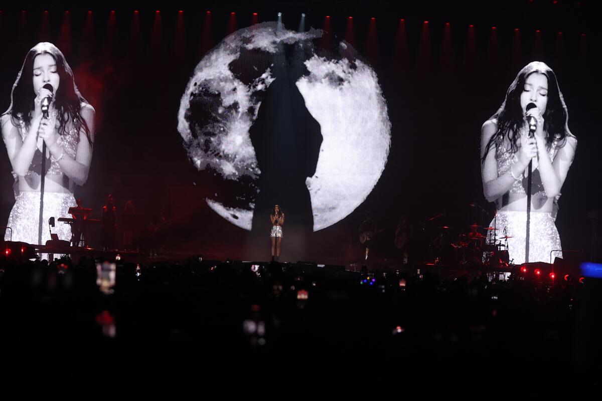 Olivia Rodrigo onstage in Palm Desert in February, her image projected on the screen behind her in stark black and white. 