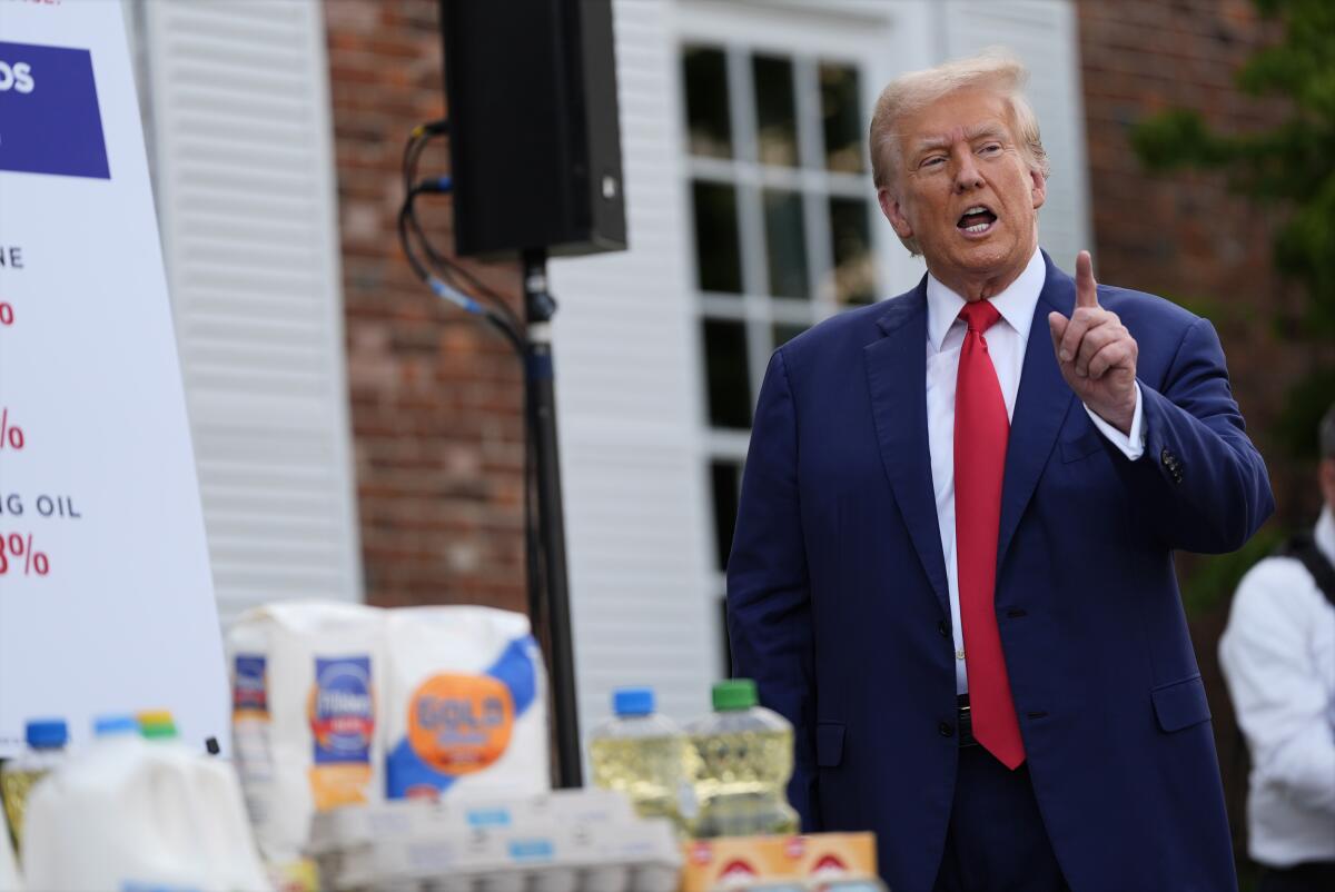 Donald Trump standing next to a table of flour and other ingredients outdoors, pointing as he speaks