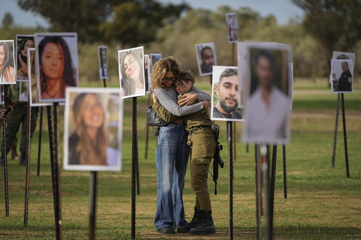 People embrace next to photos of festivalgoers killed and taken captive by militants in Israel.