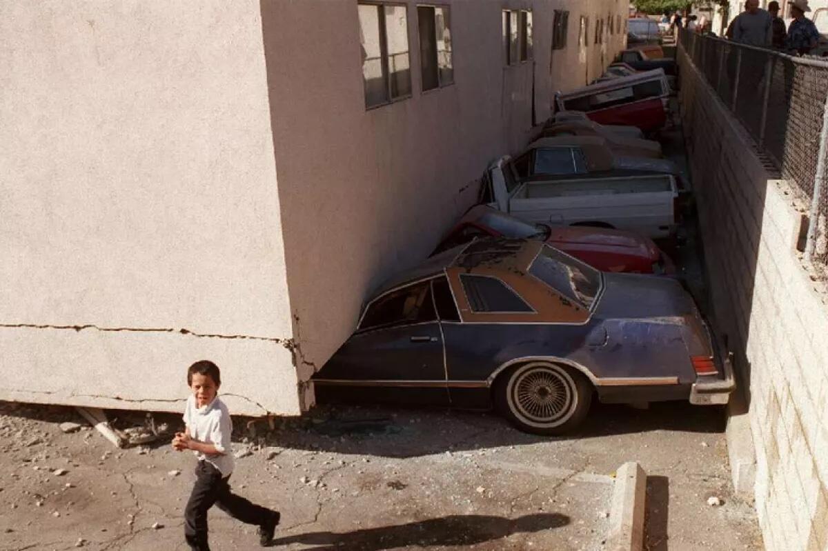 A boy runs by vehicles crushed by an apartment building that collapsed during the Northridge earthquake.