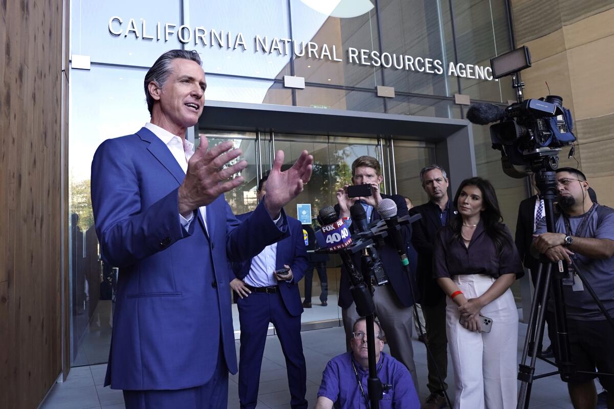 California Gov. Gavin Newsom talks to news reporters outside a building.