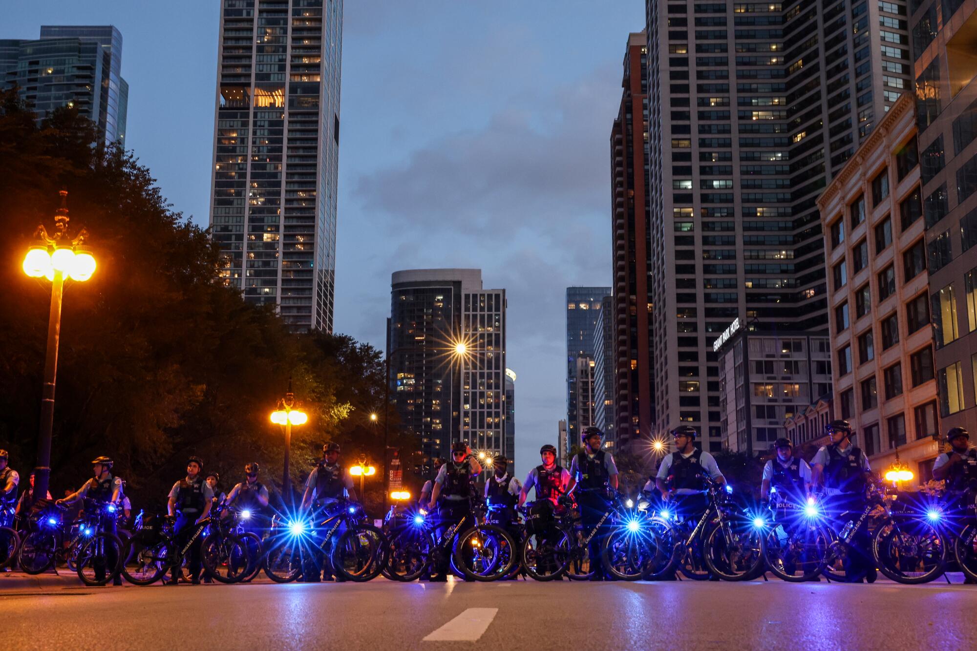 A line of police officers on bicycles with blue lights.