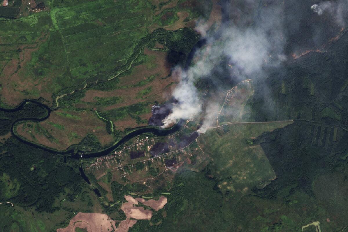 A satellite image shows smoke from fires amid green.