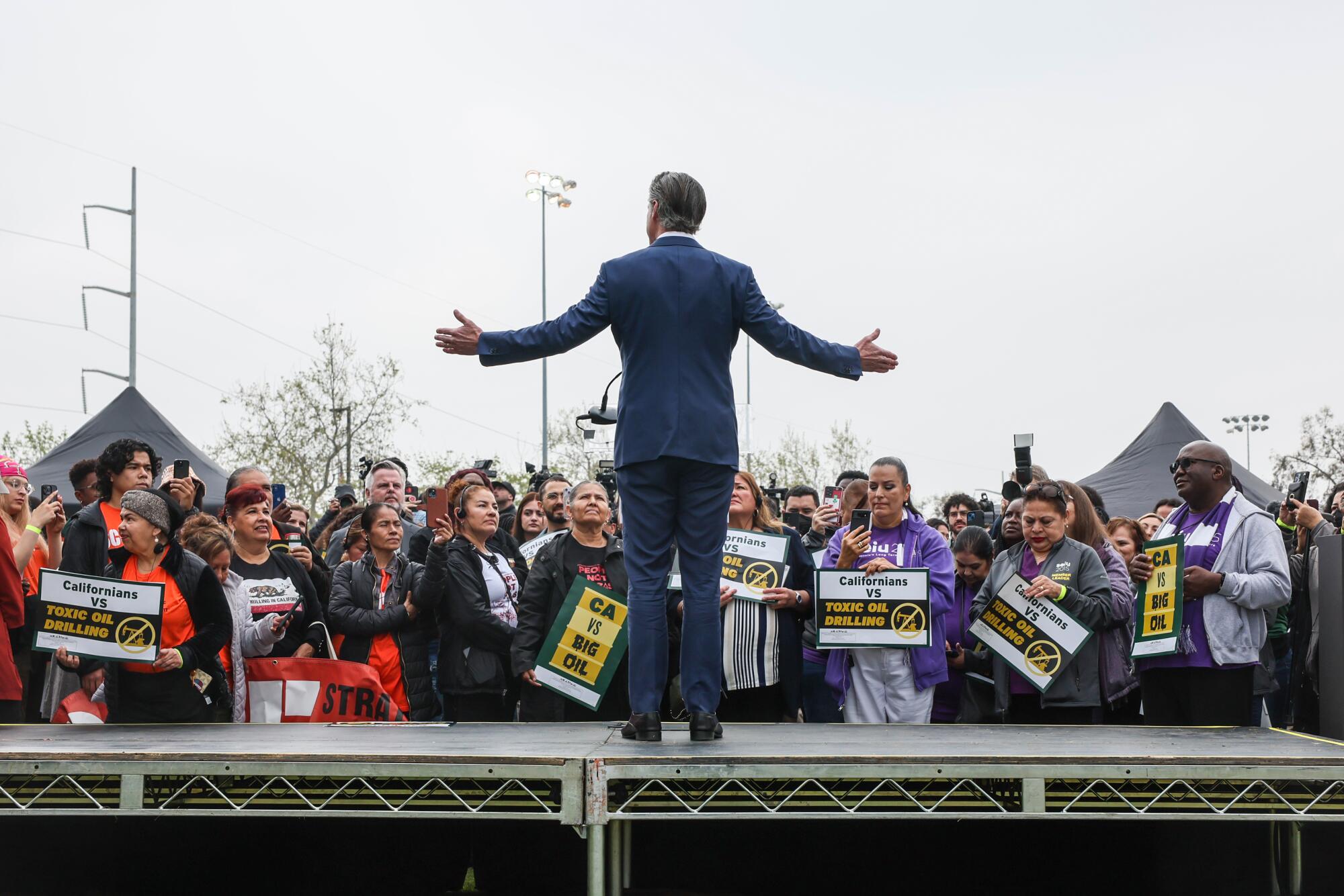 A man with arms spread speaks to people holding signs.