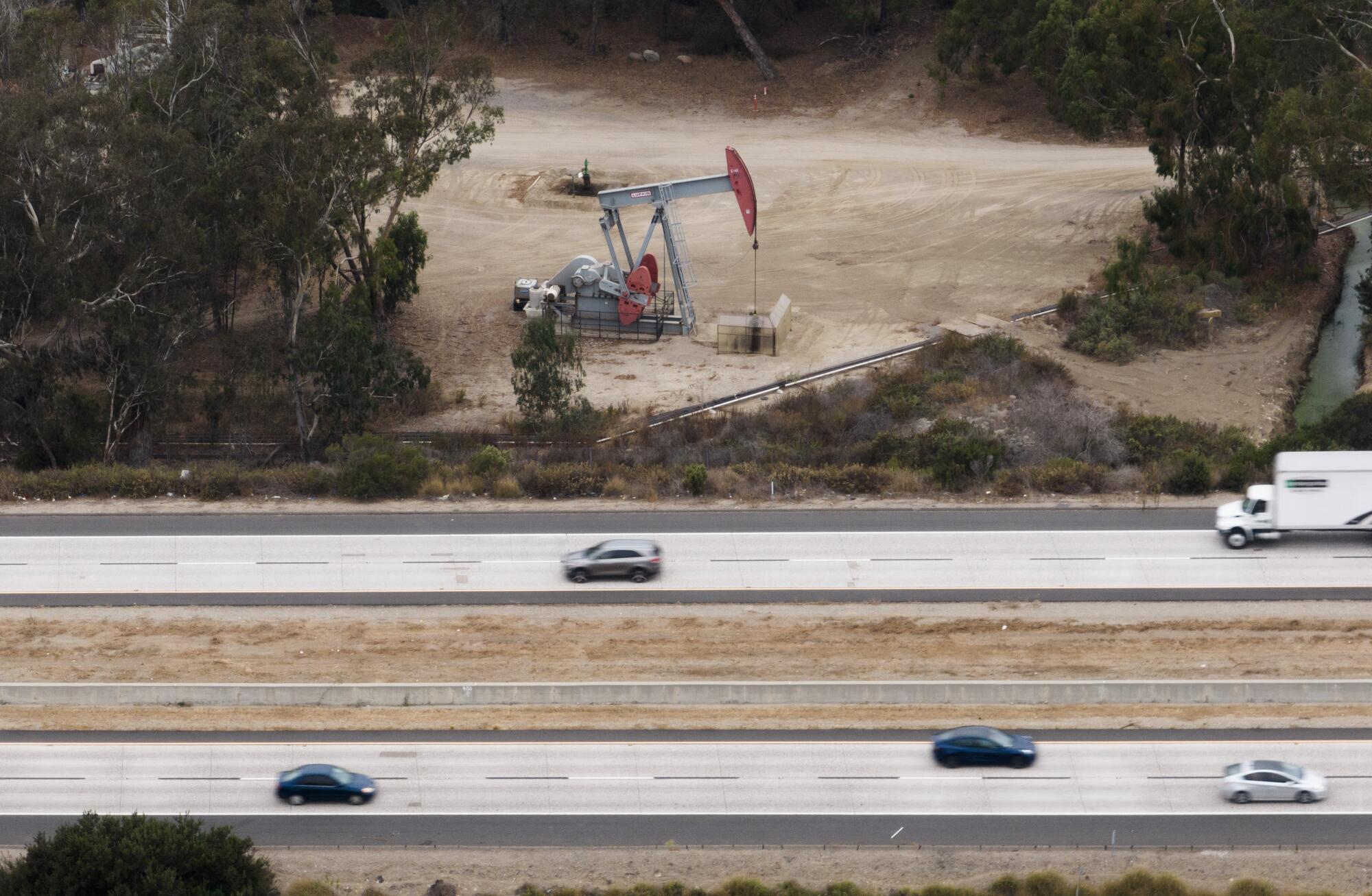 A lone oil well sits above a freeway with cars.