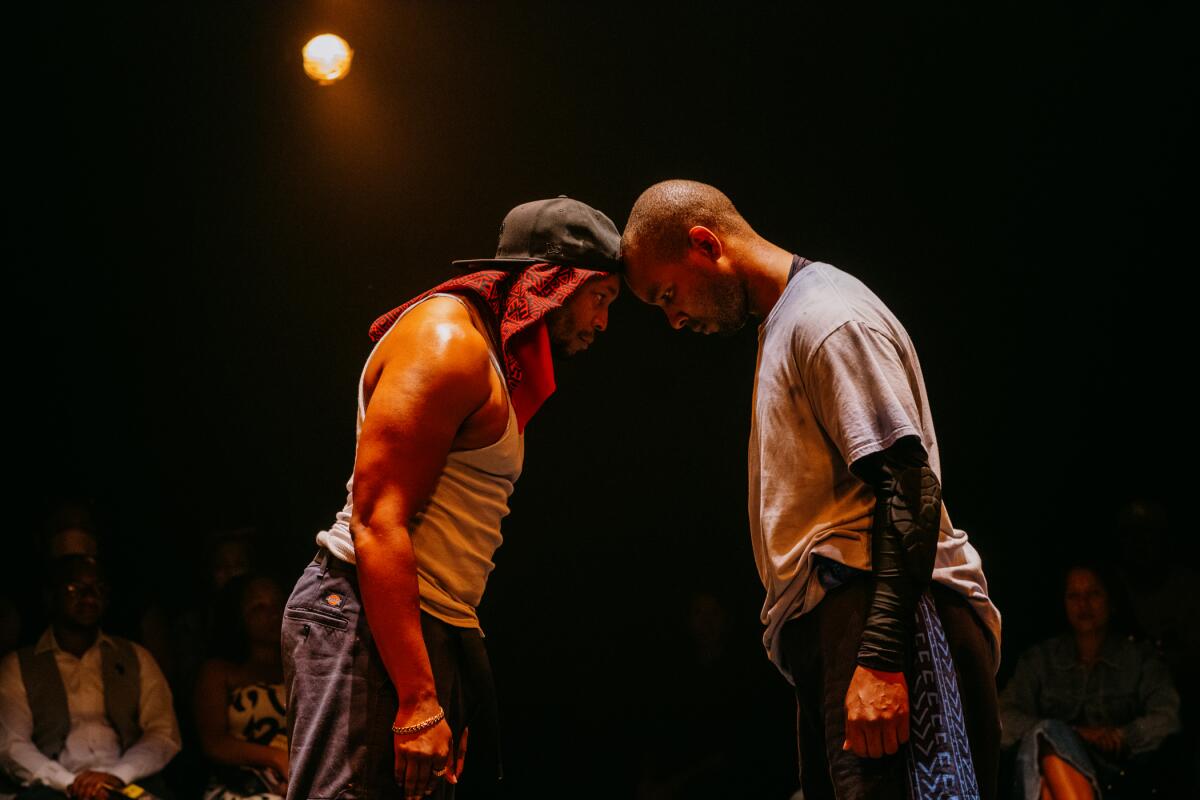 Two men lean into each other and rest their heads together on stage.