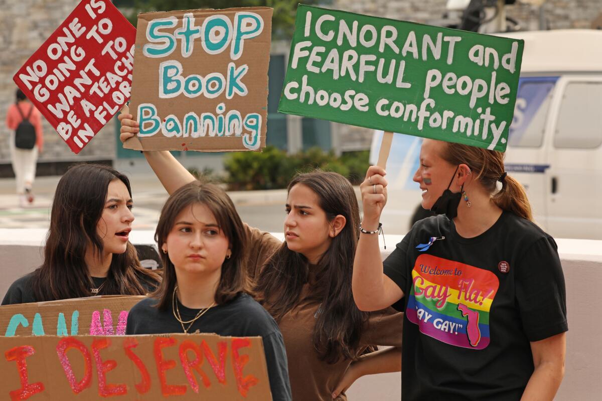 People hold signs about book bans at a school board meeting in Florida. 

