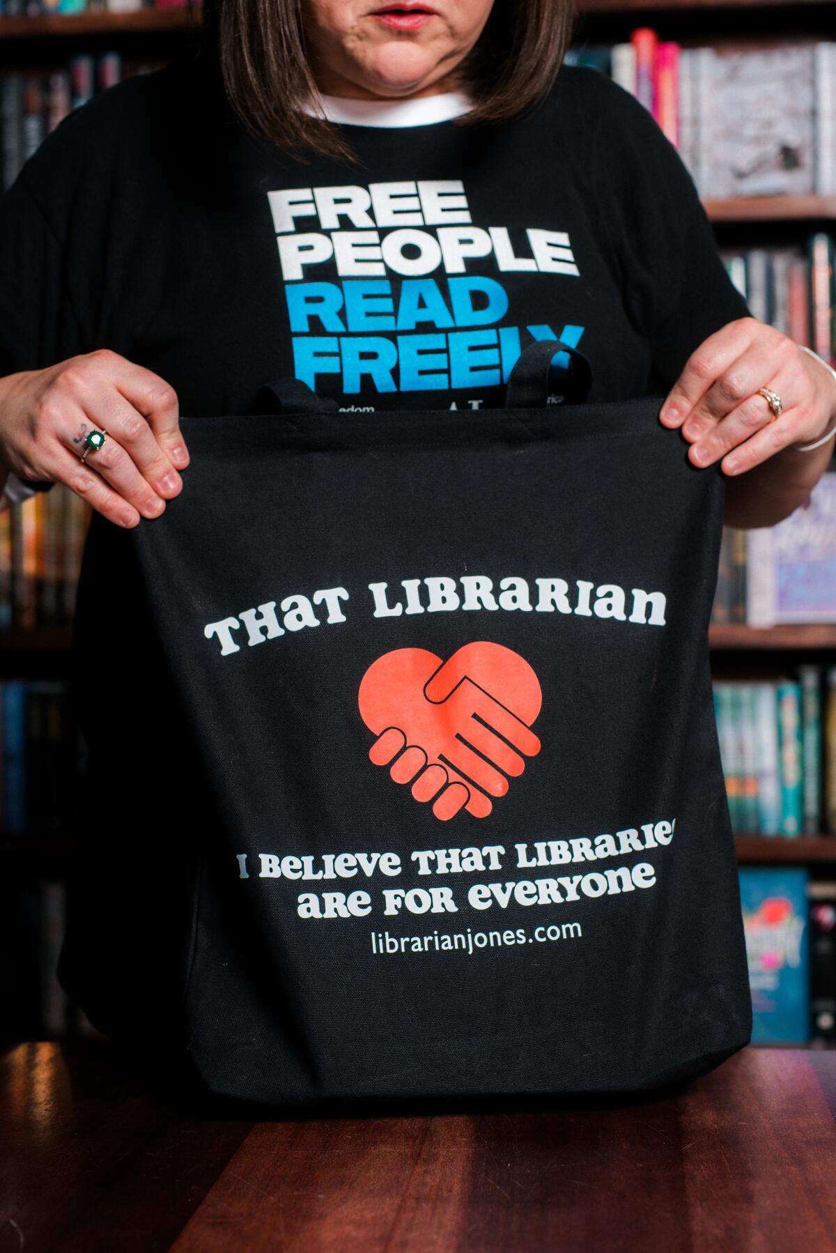 A woman holds up a dark-colored shirt that reads, "That Librarian." 