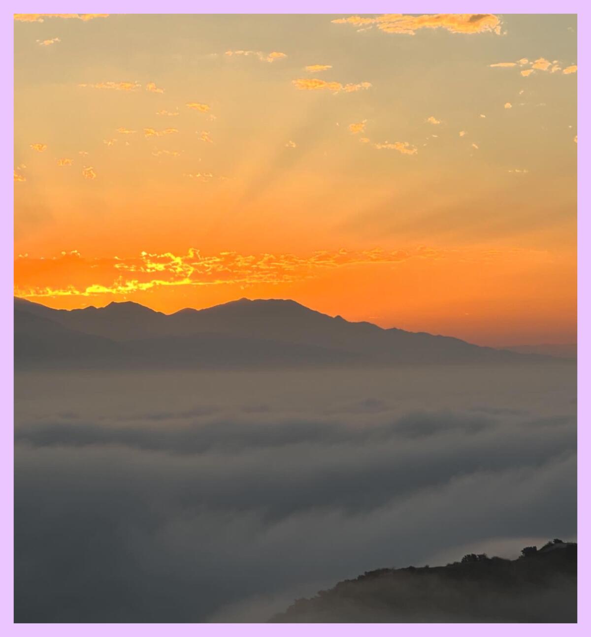 The sun rises over L.A. a mountain, illuminating a cloudy valley below.