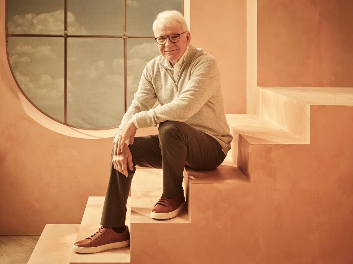 Steve Martin sits on a set of prop stairs to pose for a portrait.