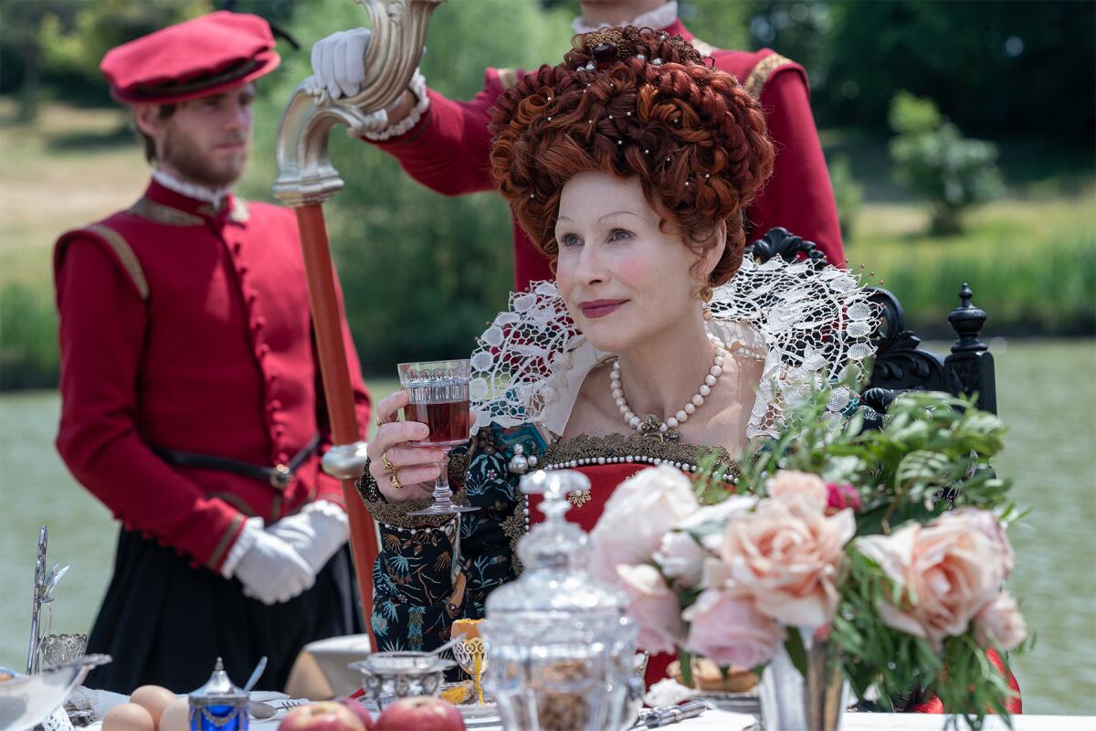 A queen drinking wine at an outdoor table, flanked by servants.