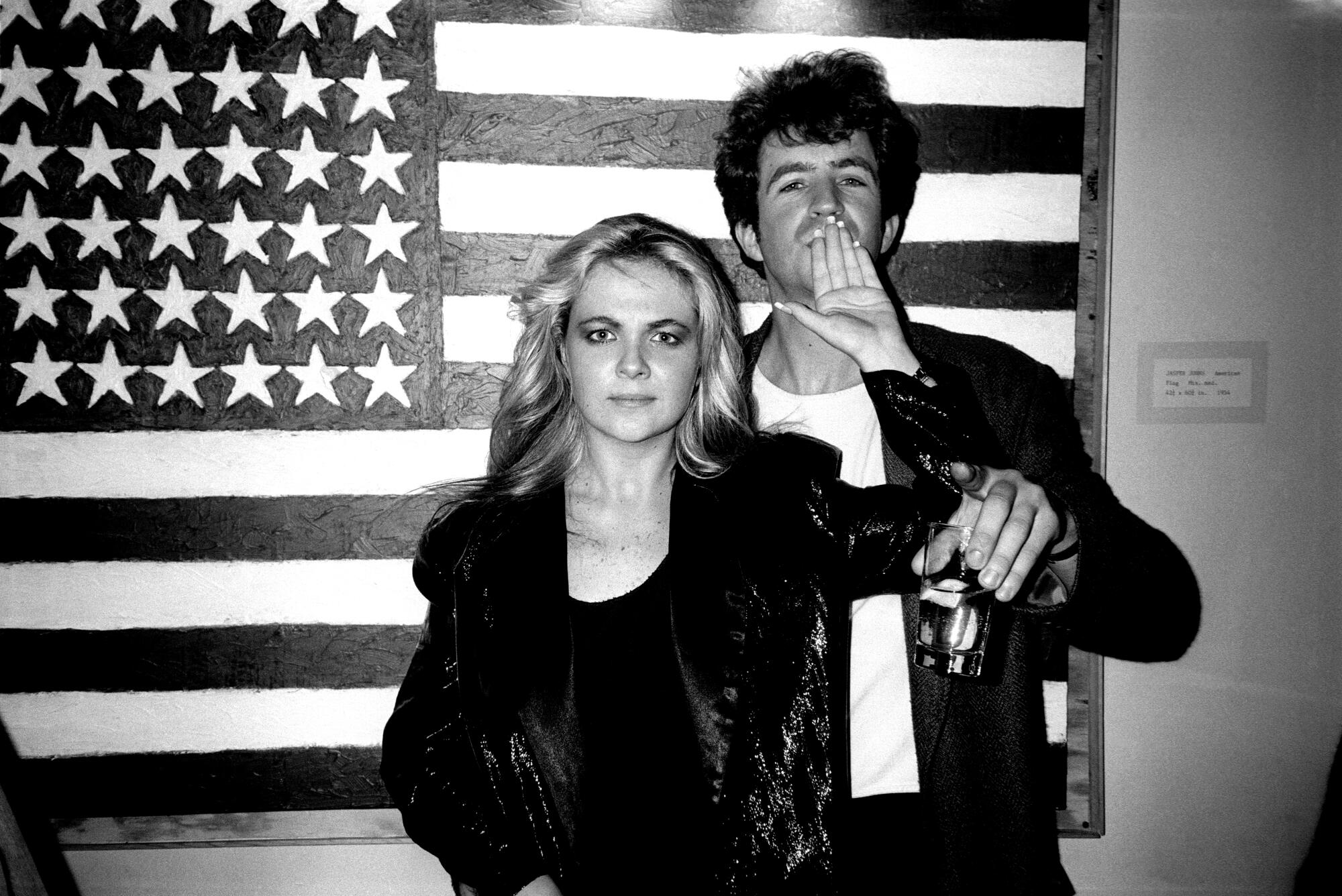 A man and a woman pose in front of an American flag in the 1980s.