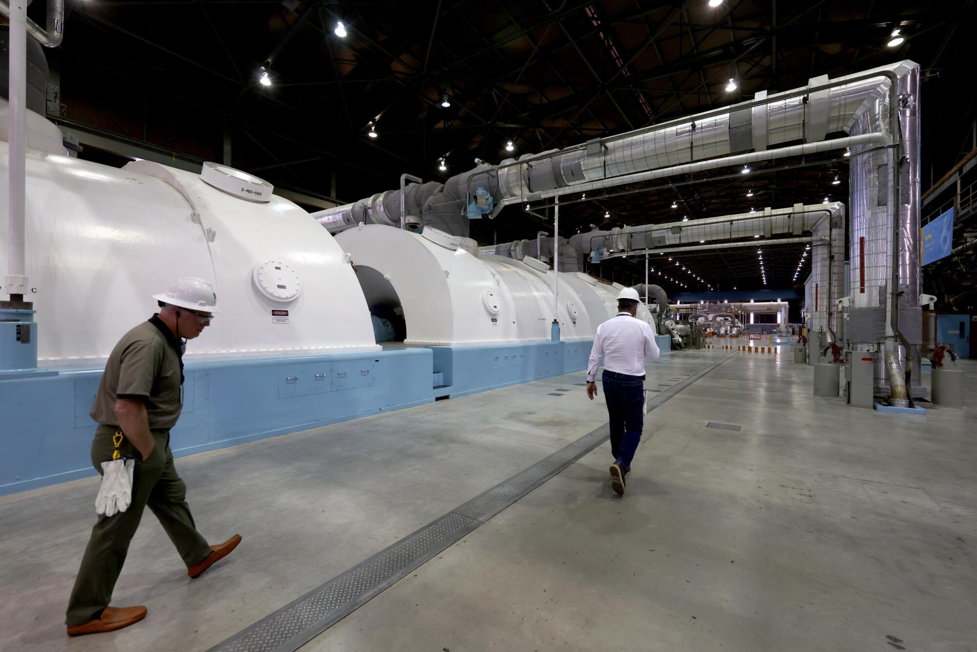 Two men walk past two massive turbine generator.