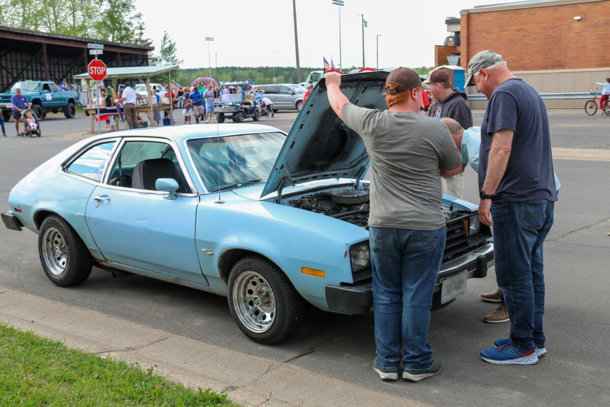 Tim Walz and others look over the engine of a light-blue Ford Pinto parked in the street as a person holds up its hood