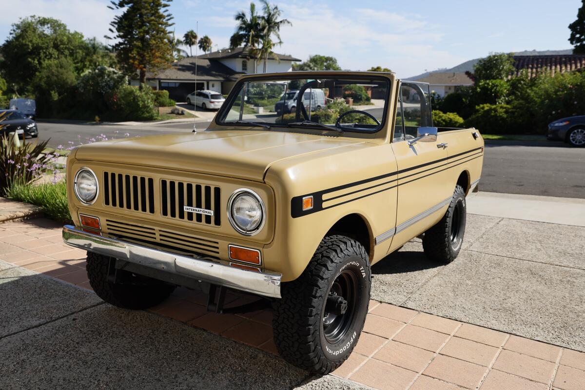 A yellow International Harvester Scout II with its top off parked in a sunny driveway