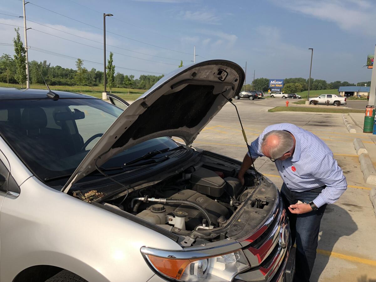 Tim Walz reaching into the engine of a newer vehicle with its hood propped open