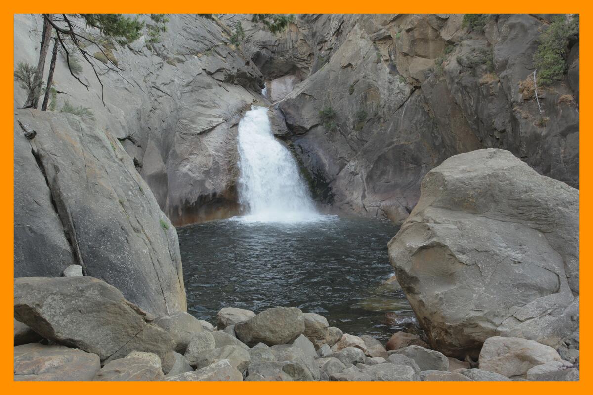 A waterfall fills a small pool surrounded by massive rocks.