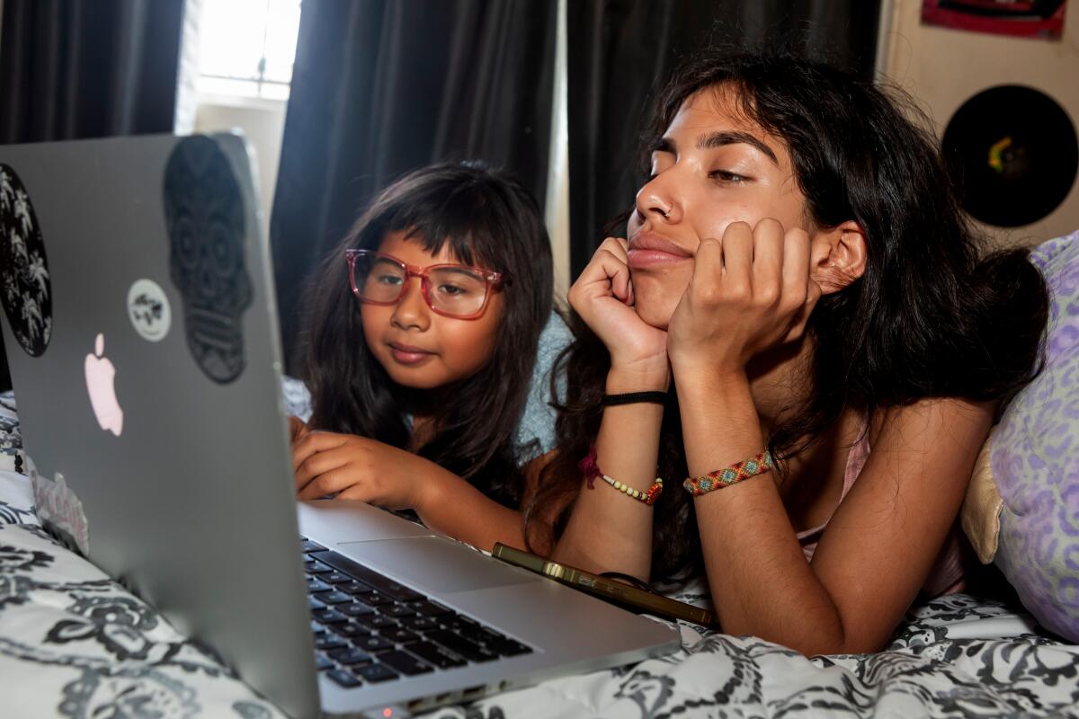 Two girls stare at a laptop screen while in bed.