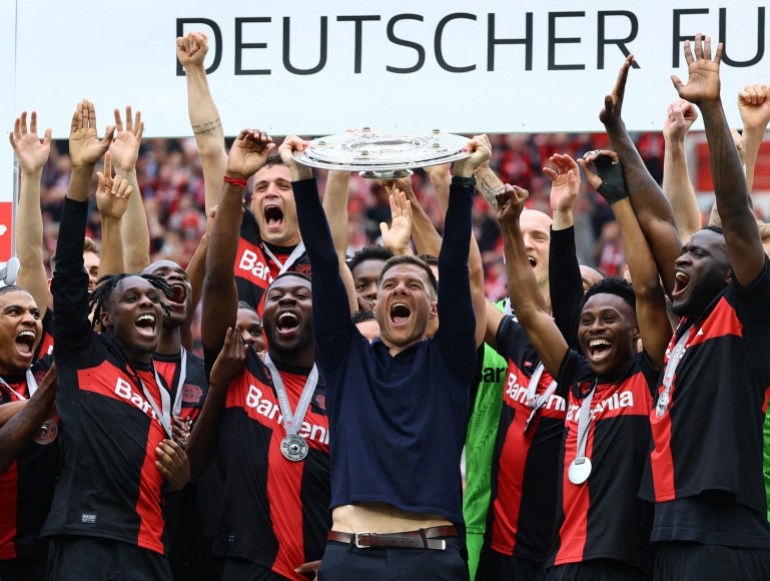 Coach holds trophy, surrounded by players.