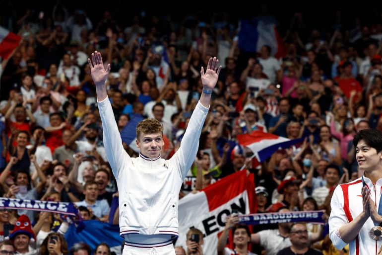 Paris 2024 Olympics - Swimming - Men's 200m Ind. Medley Victory Ceremony - Paris La Defense Arena, Nanterre, France - August 02, 2024. Gold medallist Leon Marchand of France celebrates on the podium after winning gold and setting a new Olympic record with bronze medallist Shun Wang of China. REUTERS/Clodagh Kilcoyne