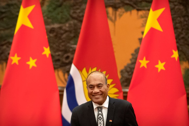 Kiribati's President Taneti Maamau. He is standing in front of Kiribati and Chinese flags. He is smiling.