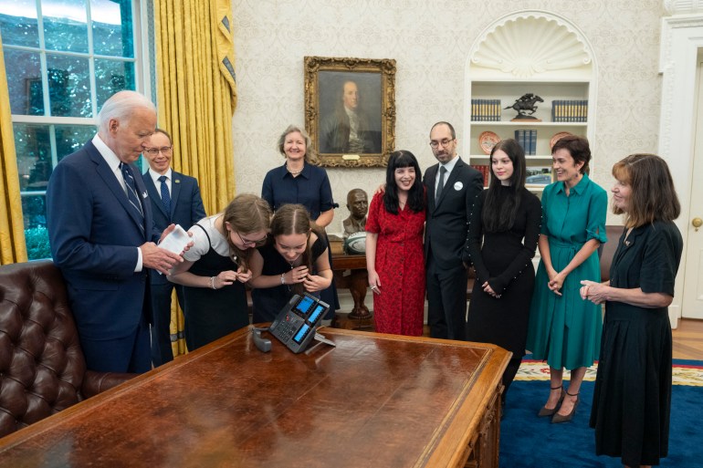 Biden with some of the freed prisoners' relatives in Oval Office at the White House. Two girls, the daughters of journalist Alsu Kurmasheva, are speaking into a phone on the desk. Everyoe looks very happy.