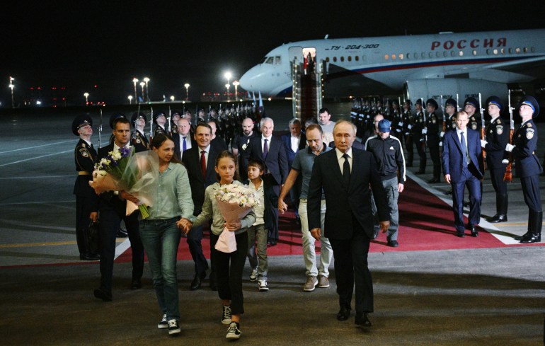 Putin walking with Russians freed in the prisoner swap at Moscow airport. It' dark. The plane is behind them.