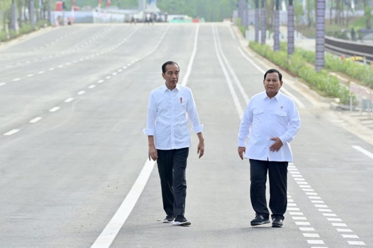 Joko Widodo and Prabowo Subianto walk along a multi-lane deserted highway