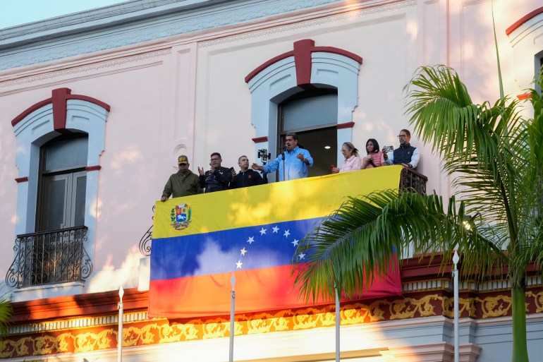 Nicolas Maduro greets supporters from a flag-draped balcony at the Miraflores presidential palace in Caracas.