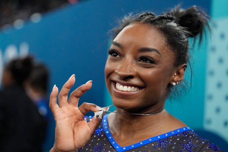 Simone Biles, of the United States, celebrates with her GOAT necklace after winning the gold medal during the women's artistic gymnastics all-around finals in Bercy Arena at the 2024 Summer Olympics, Thursday, Aug. 1, 2024, in Paris, France. (AP Photo/Charlie Riedel)