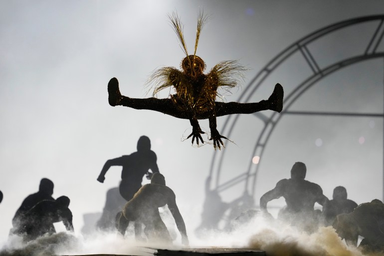 Dancers perform at the closing ceremony in Paris. One is doing a high leap into the air. Others are crouching down. There is lots of white smoke