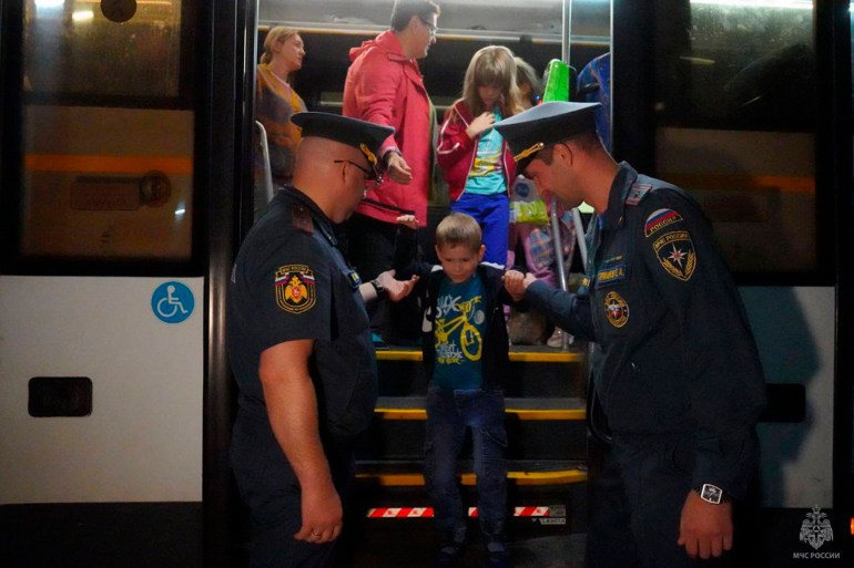 A boy getting off a bus and being held down the steps by two police officers standing at the door.