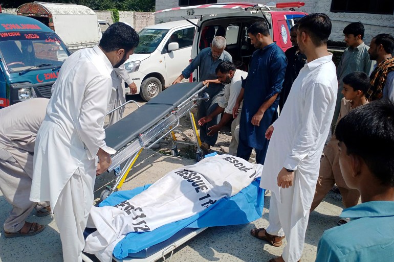 Volunteers and relatives prepare to load the body of a woman, who was killed as a passenger bus fell into a ravine, into an ambulance at a hospital in Kahuta, Pakistan