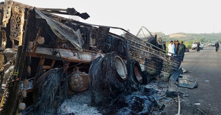 People look burnt vehicles, torched by gunmen after killing passengers, at a highway in Musakhail