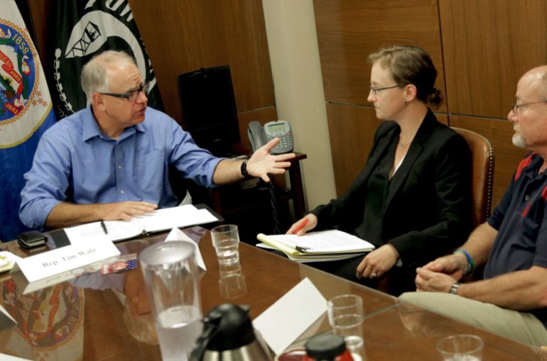 Tim Walz gestures across a wooden table, as he speaks with Melissa Houghtaling about veterans' mental health