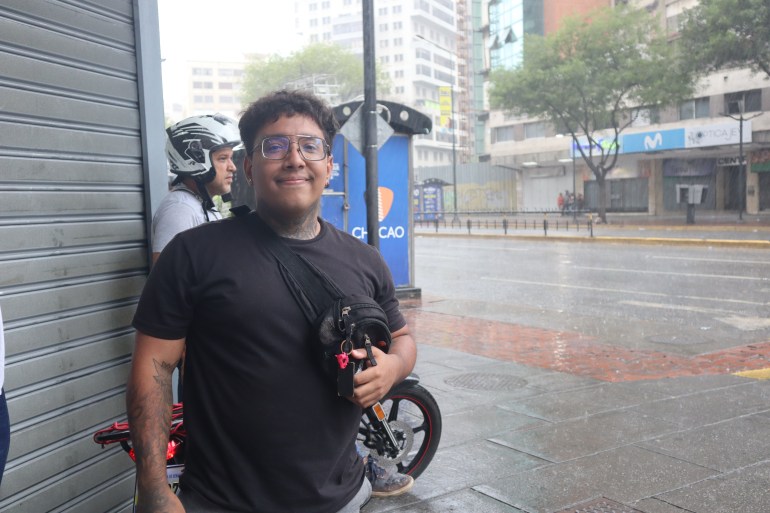 Cristian José Camacaro Guevara stands under an awning as rain pours on the street in Caracas.