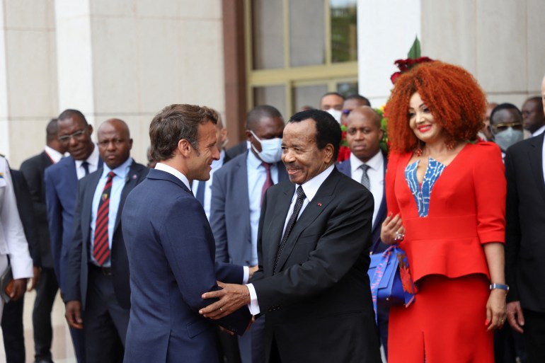 Cameroon's President Paul Biya shakes hands with French President Emmanuel Macron as Biya's wife Chantal looks on, after their meeting at the presidential palace, in Yaounde, Cameroon, July 26, 2022