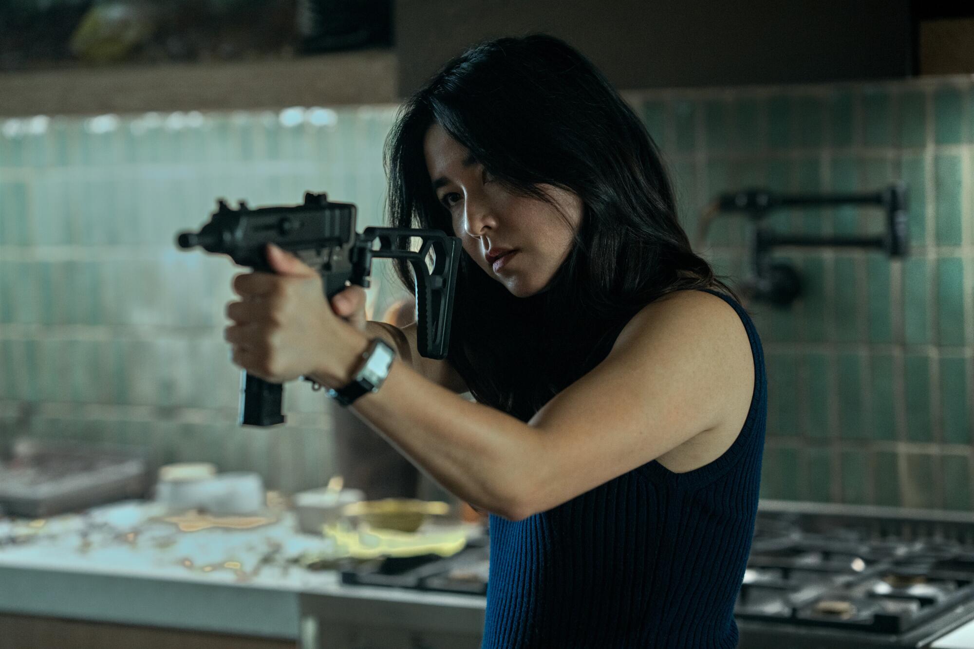 Maya Erskine stands in a kitchen aiming a gun in a scene from "Mr. & Mrs. Smith."