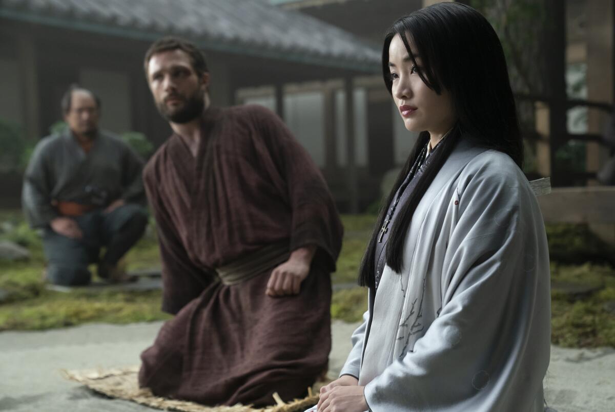 A man and a woman in kimonos kneel on mats in a garden in "Shogun."