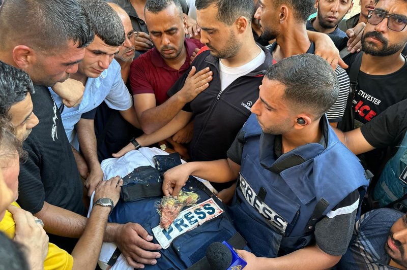 Mourners, colleagues and fellow journalists examine a tattered press jacket that surrounded the body of Al-Jazeera Arabic journalist Ismail Al-Ghoul, killed along with his cameraman Rami Al-Refee, in an Israeli airstrike on Tuesday. Photo by Hossam Azzam/UPI