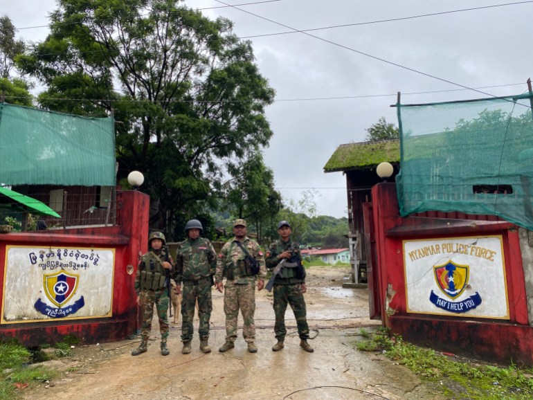 Anti-coup fighters standing at the entrance to a Myanmar police station. The gates are open. It looks like it's been raining.